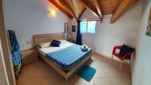A bedroom with a wooden ceiling, a bed with a patterned bedspread, a red chair, and a blue rug. - Holiday Properties Soleil (Santa Maria)