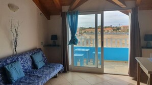 A room with a wooden ceiling, a sofa with blue cushions, a table, and a view of a blue balcony with chairs. - Holiday Properties Soleil (Santa Maria)