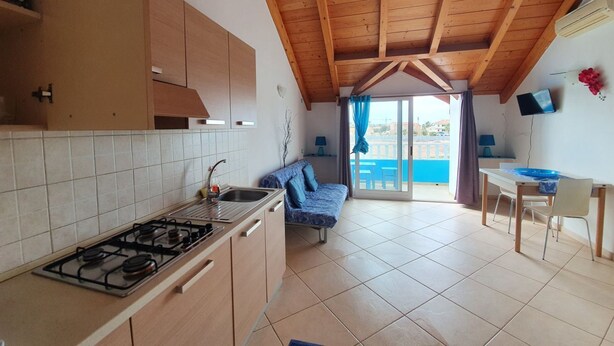 A kitchen with a gas stove, wooden cabinets, and a dining area with a table and chairs. - Holiday Properties Soleil (Santa Maria)