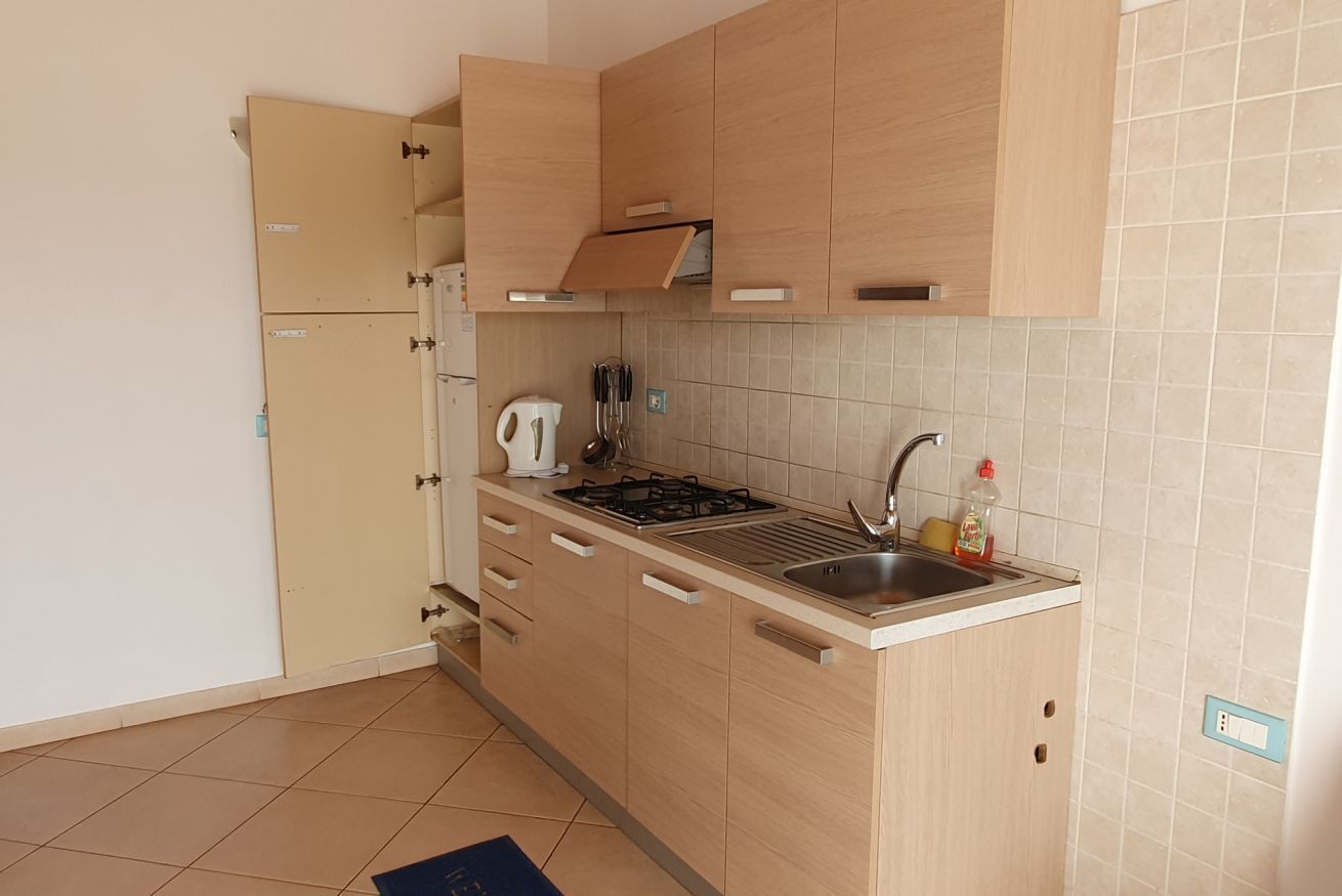 A compact kitchen with light wooden cabinets, a built-in gas stove, a sink, and a kettle.