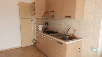 A compact kitchen with light wooden cabinets, a built-in gas stove, a sink, and a kettle.