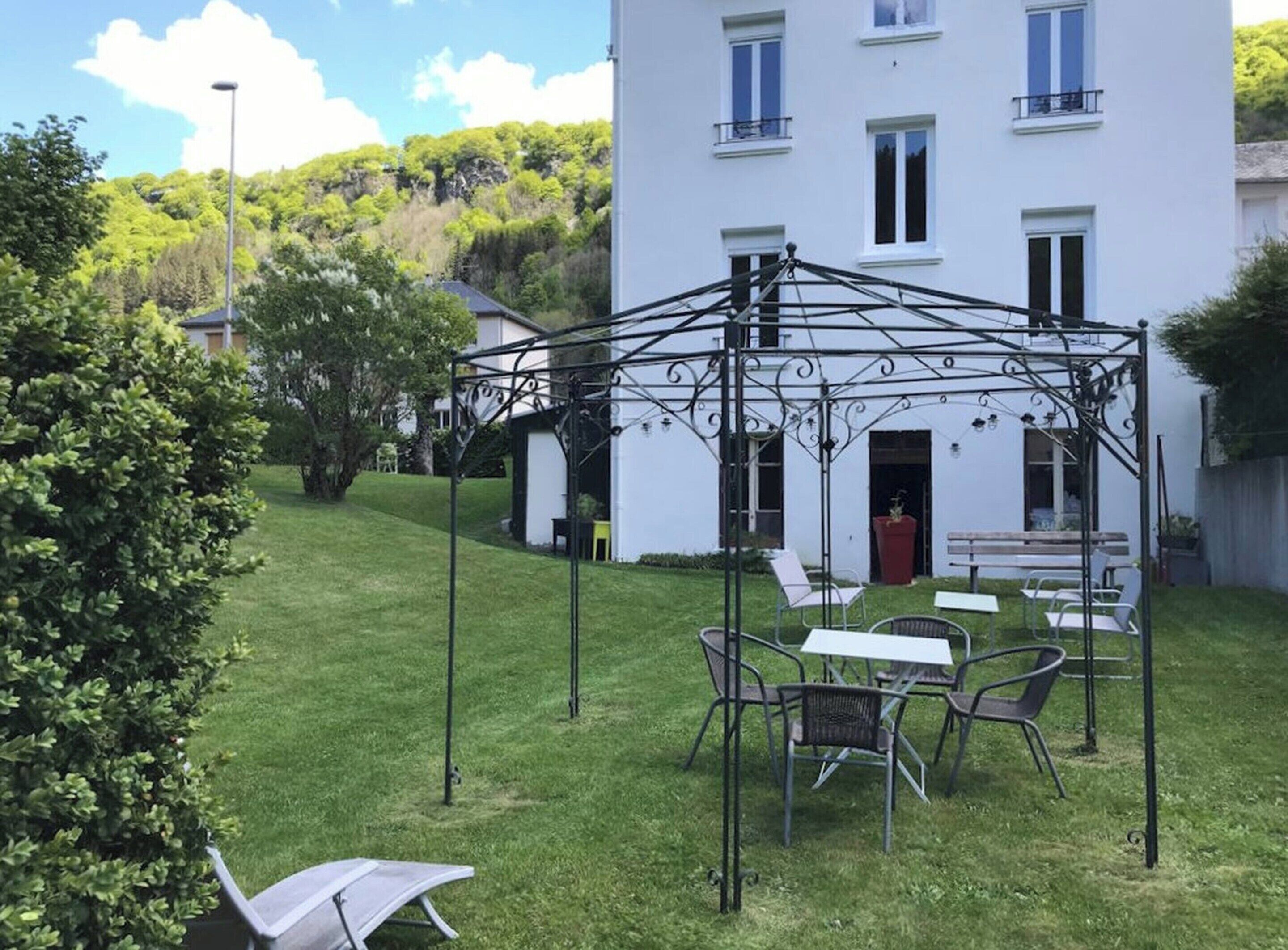 Un bâtiment blanc doté d’un espace extérieur abrité avec des sièges, entouré de verdure et d’une pelouse bien entretenue.