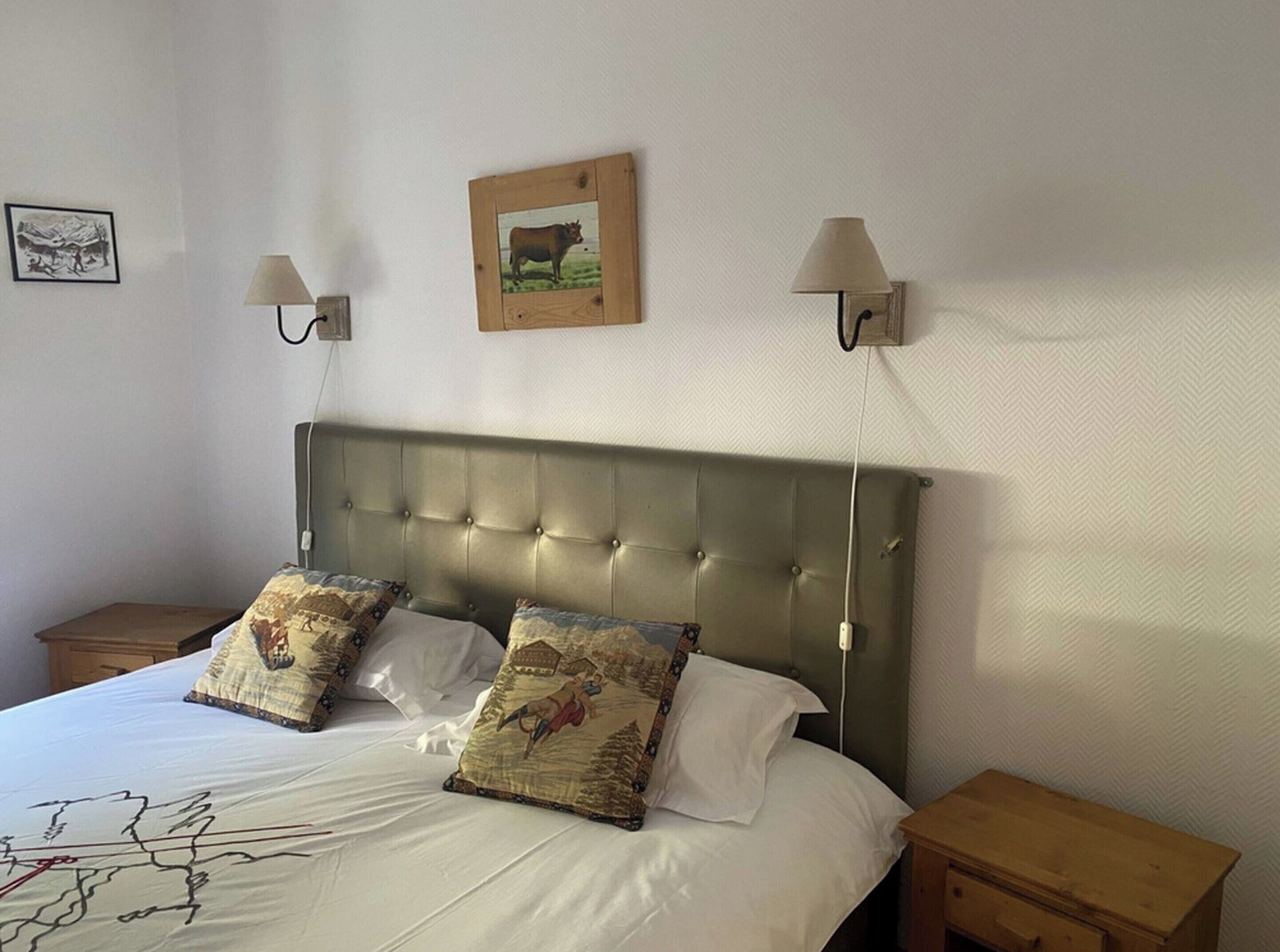 A bedroom with a large bed, two nightstands, a headboard, wall-mounted lamps, and a framed picture on the wall.