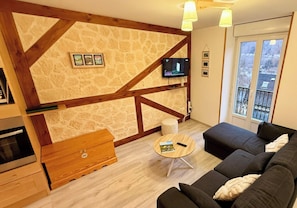 Ein Wohnzimmer mit Steinwand, Holzbalken, Fernseher, Sofa, Couchtisch und einem Fenster mit Blick.