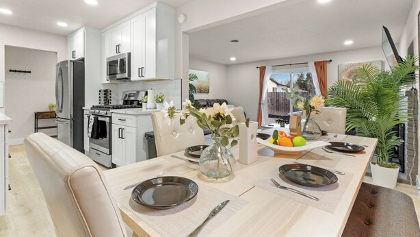 Cocina moderna con armarios blancos, un refrigerador de acero inoxidable y un microondas. Hay una mesa de comedor puesta con platos y un jarrón de flores.