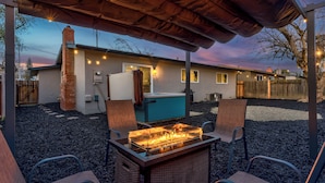 Un patio exterior cubierto con una chimenea, asientos y una casa al fondo.