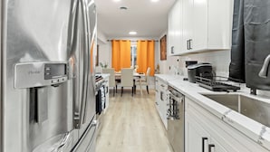 Una cocina moderna con electrodomésticos de acero inoxidable, dispensador de agua y un comedor con cortinas anaranjadas.