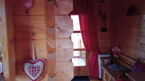 A cozy cabin interior with wooden walls, a heart-shaped decoration, a bench, and a small table. - Roulotte La passe pierre En baie de Somme (Pendé)
