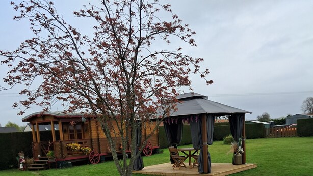 A gazebo with a table and chairs, surrounded by a well-maintained lawn and a gravel path. - Roulotte La passe pierre En baie de Somme (Pendé)