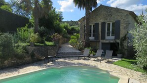 Una piscina de piedra con sillas reclinables y una escalera de piedra que conduce a un edificio con balcón.