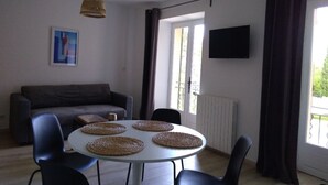 Una sala de estar con sofá, una mesa redonda con individuales, televisor y ventana con cortinas.
