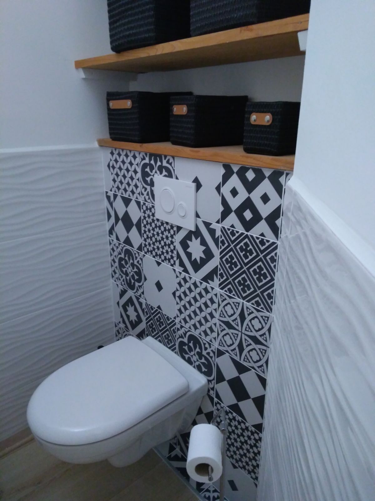A small, compact bathroom with a white toilet, patterned tiles, and a shelf with storage boxes.