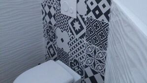 Un baño pequeño y funcional con inodoro blanco, baldosas con estampado y un estante con cajas de almacenamiento.