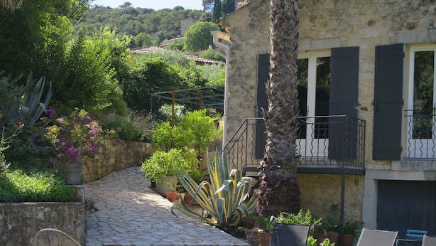 Edificio de piedra con piscina, mobiliario exterior y abundante vegetación.