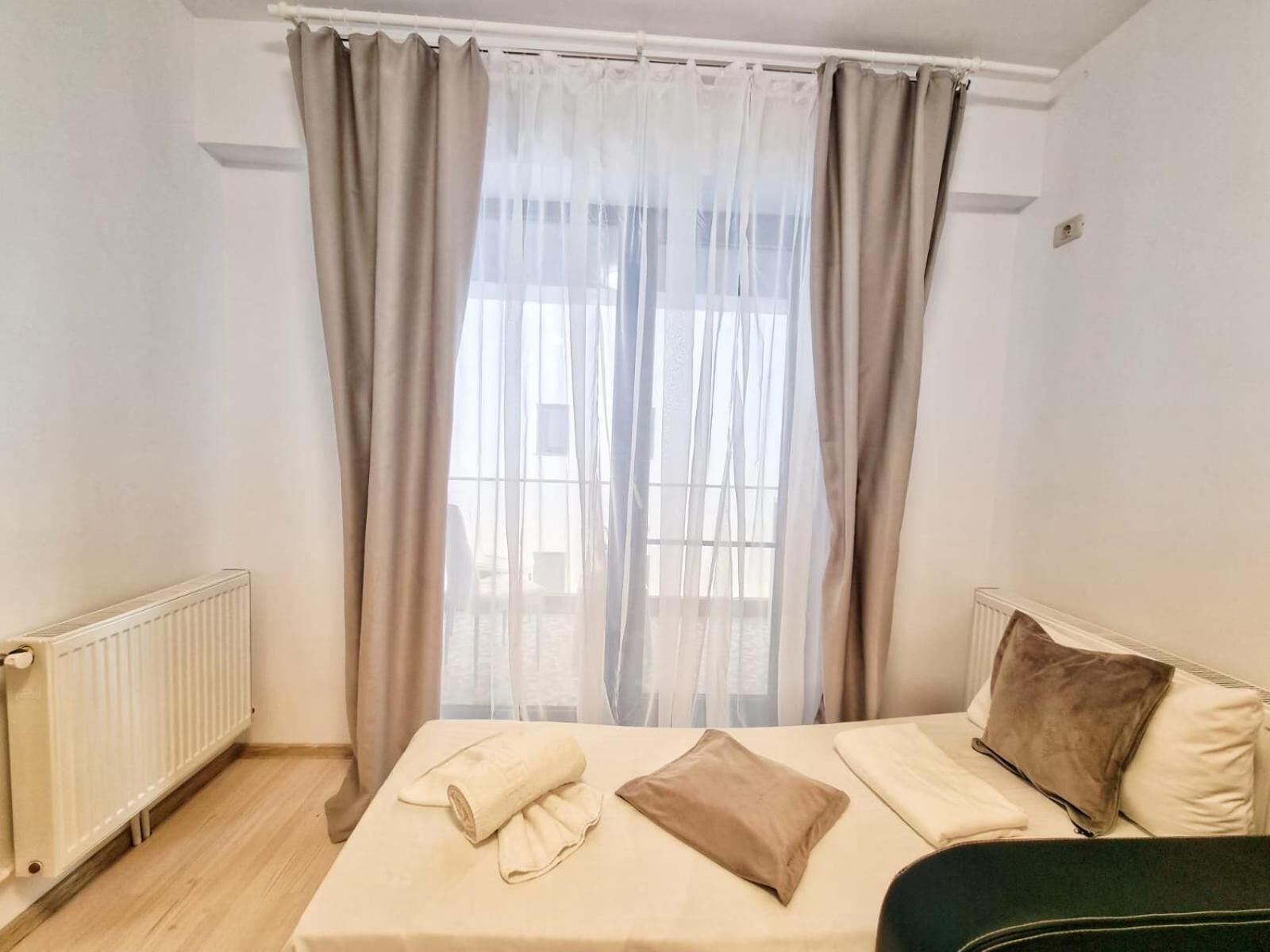 Un dormitorio con cama, radiador y cortinas translúcidas.