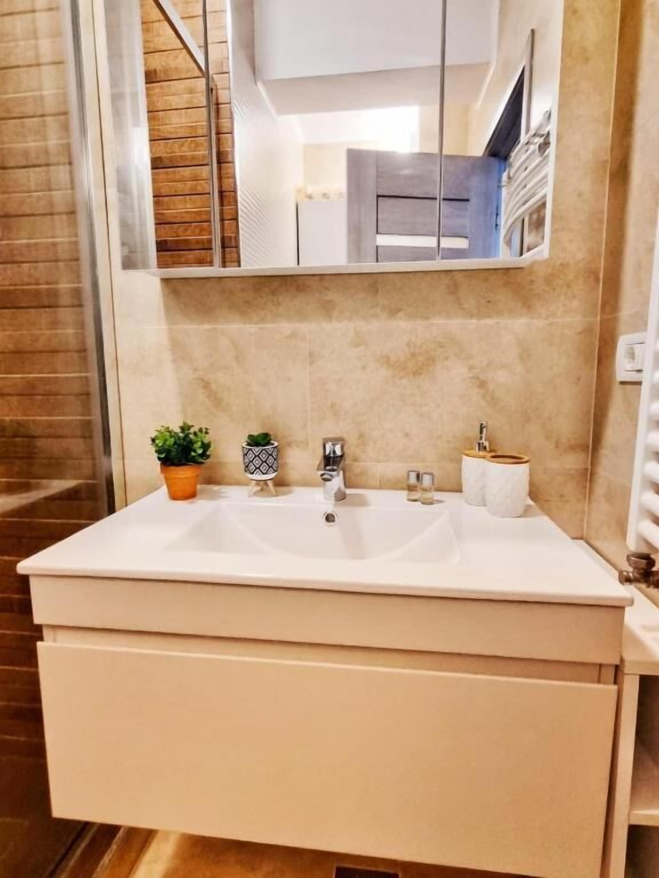 A bathroom with a white sink, two faucets, a mirror above the sink, and a wooden floor.