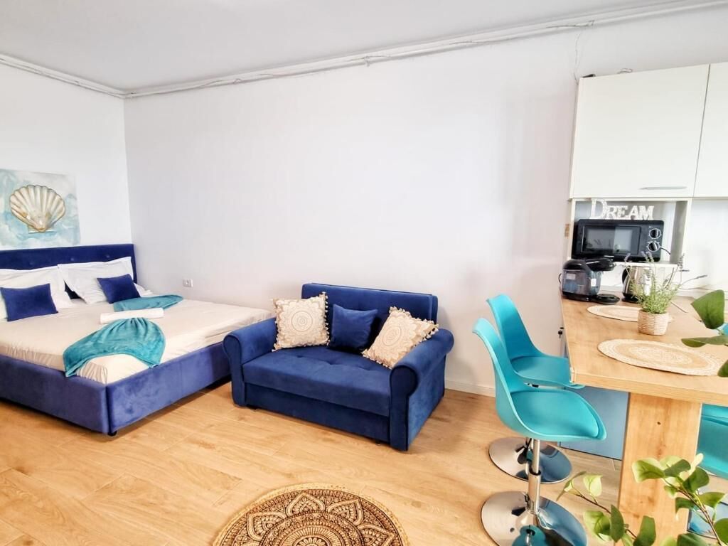 A bedroom with a bed, a blue sofa, a desk with a chair, and a microwave.