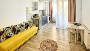 Un apartamento moderno con un sofá amarillo, una mesa de comedor y una cocina al fondo.