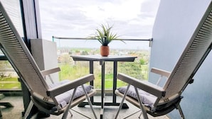 Un balcón con dos sillas, una mesita pequeña, una planta en maceta y vista panorámica de la ciudad.