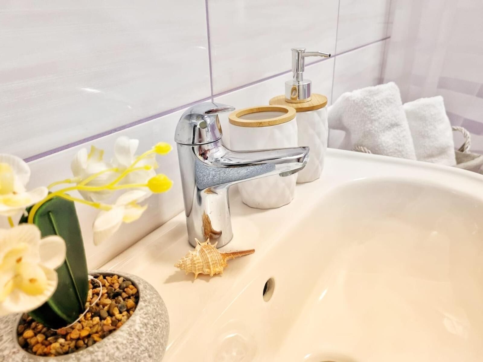 Un lavabo de baño con un grifo moderno, una pequeña concha decorativa y una planta en maceta.