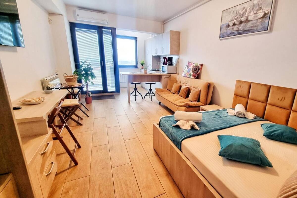 A modern apartment with a large bed, a sofa, a dining area, and a kitchen.