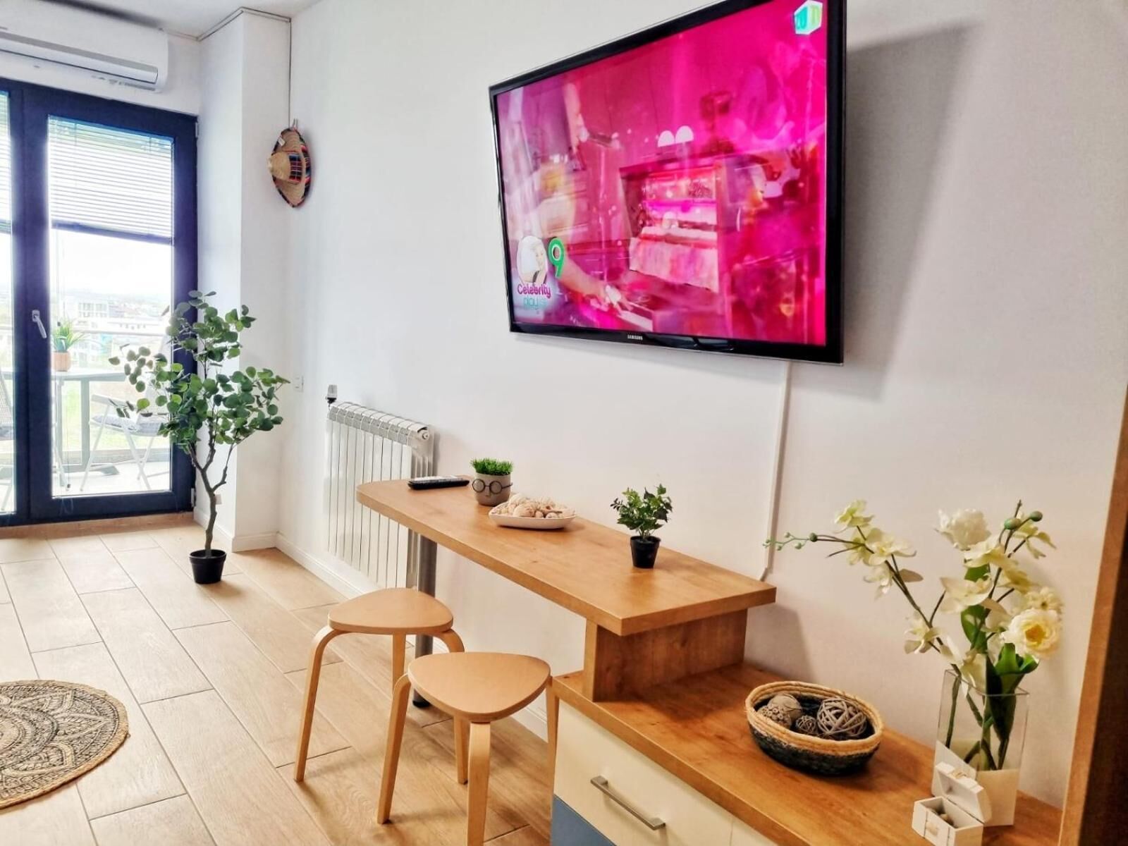 A modern living room with a flat-screen TV, wooden furniture, and potted plants.