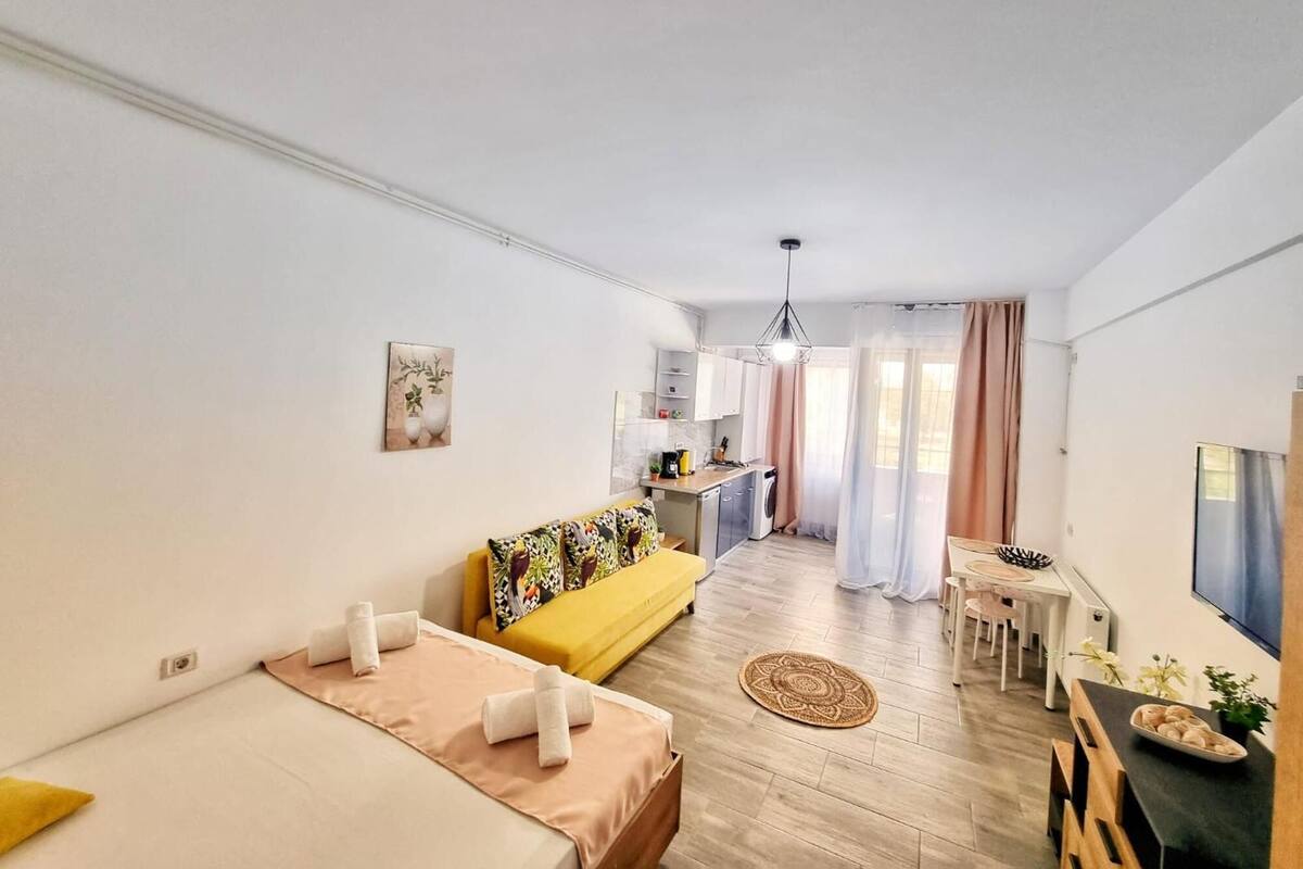 A modern, well-lit room with a sofa, a bed, a small kitchen area, and a dining table.