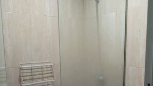 Um chuveiro pequeno e fechado com porta de vidro, um porta-toalhas de metal e um vaso sanitário.