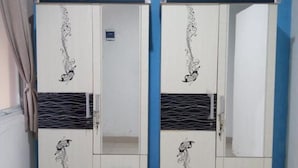 Quarto com dois armários brancos encostados numa parede azul, cada um com um detalhe decorativo e um pequeno espelho.