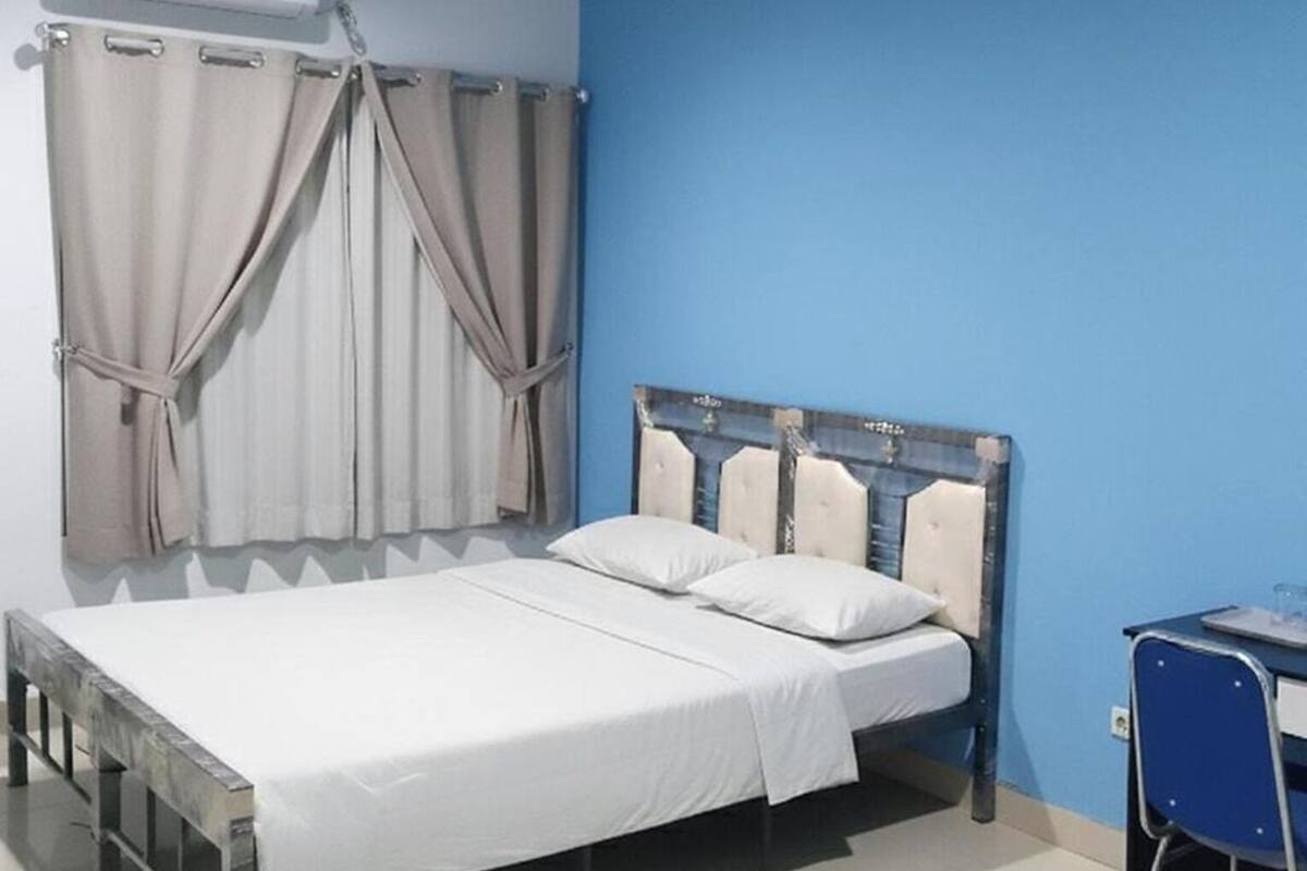A bedroom with a bed, curtains, a desk, and an air conditioning unit.