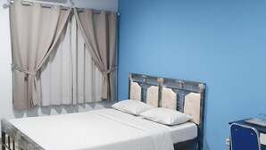 Quarto com cama, cortinas, escrivaninha e ar condicionado.