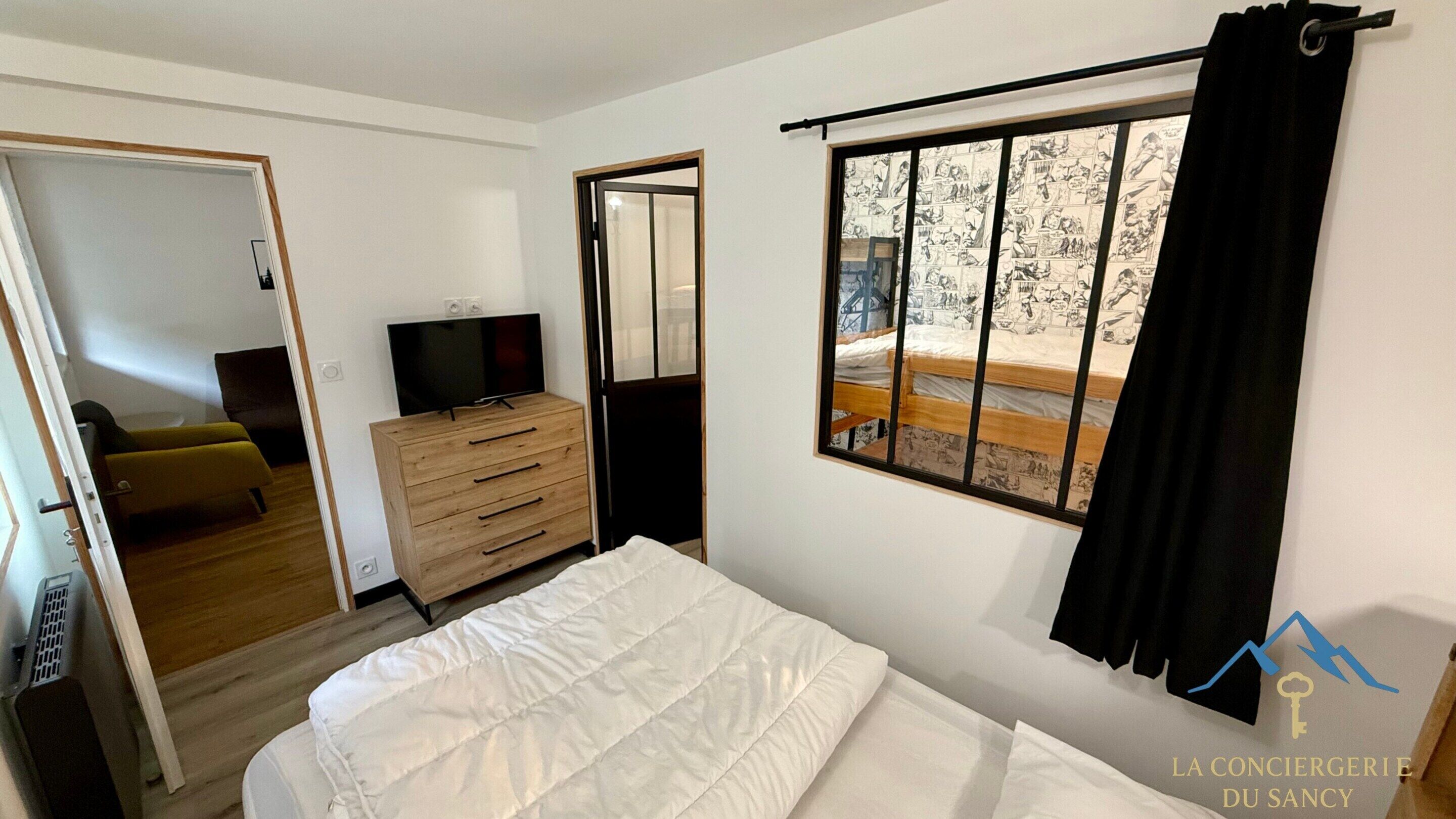 Quarto com cama, cômoda, televisão e janela com cortinas.