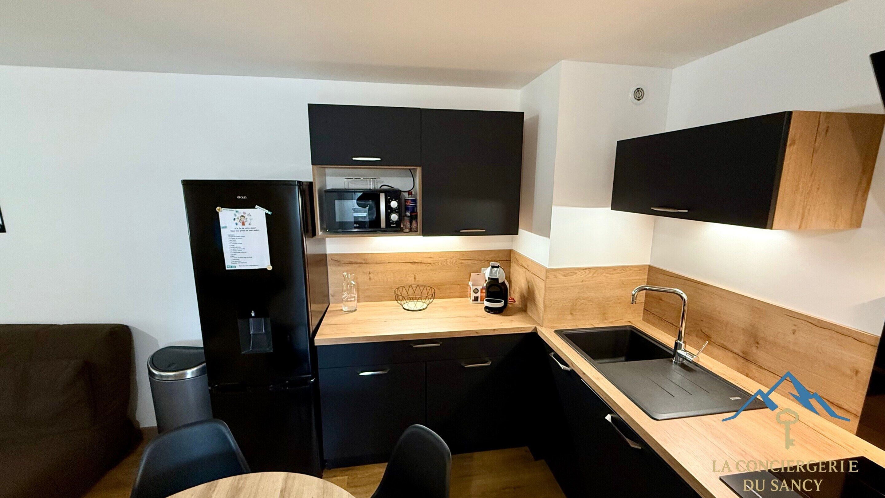 A compact kitchenette with a refrigerator, microwave, and sink. There is a wooden countertop and a small dining area with a table and chairs.