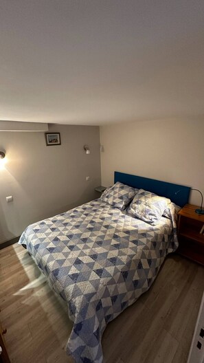 A bedroom with a bed, a nightstand, a wall-mounted lamp, and a small picture on the wall. - Charming Mont-dore Duplex Stay (Mont-Dore)