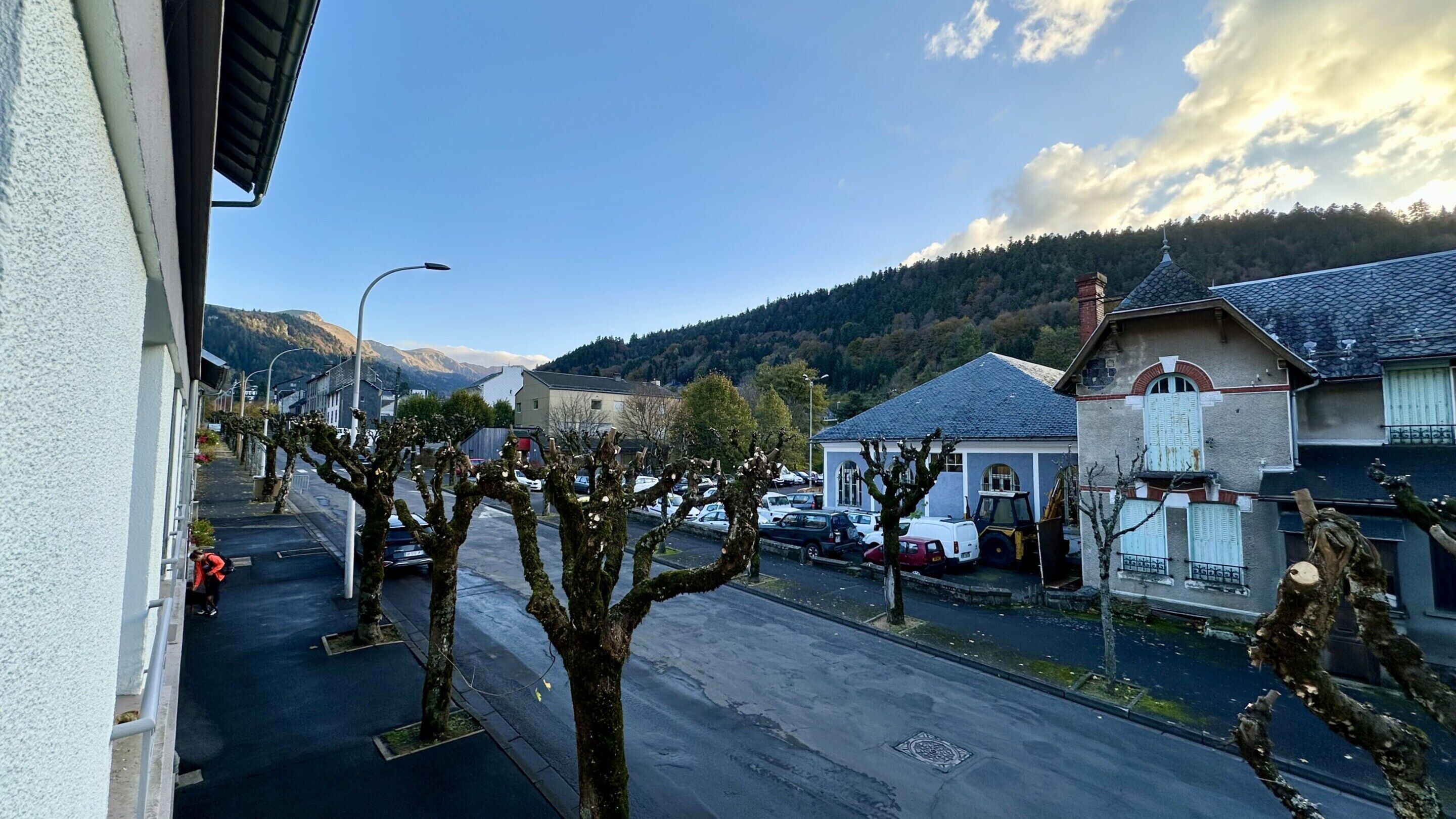 A street view with residential buildings, parked cars, and a clear sky.