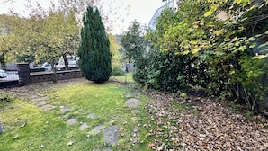 A garden with a stone pathway, a tall coniferous tree, and a hedge. - Sancy Refuge by the Snowy Peak (Mont-Dore)