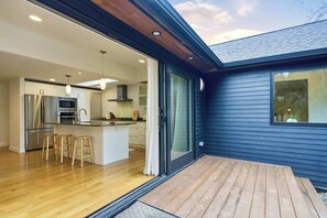 A modern kitchen with a central island, wooden stools, and a sliding glass door leading to a deck. - Elegant 3B House near UW, Remodeled & EV Parking (Seattle)