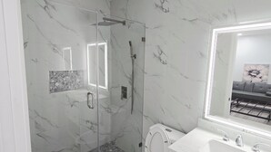 Een badkamer met een douchecabine van glas, een toilet en een wastafel met spiegel.