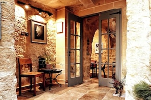 A rustic interior with stone walls, a wooden bench, a table with a plant, and a framed picture. - Casa Jorge (Victoria)