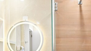 Casa de banho com espelho redondo, secador de cabelo e chuveiro.