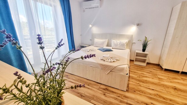 A modern bedroom with a wooden bed, a bedside table, a nightstand, and a potted plant. - Casa Cochilia-Camere de inchiriat (Eforie Nord)