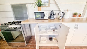 A kitchen with a stove, oven, microwave, and a small cabinet with dishes. - Casa Cochilia-Camere de inchiriat (Eforie Nord)