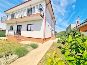 A two-story residential building with a balcony, a staircase, and a garden area.