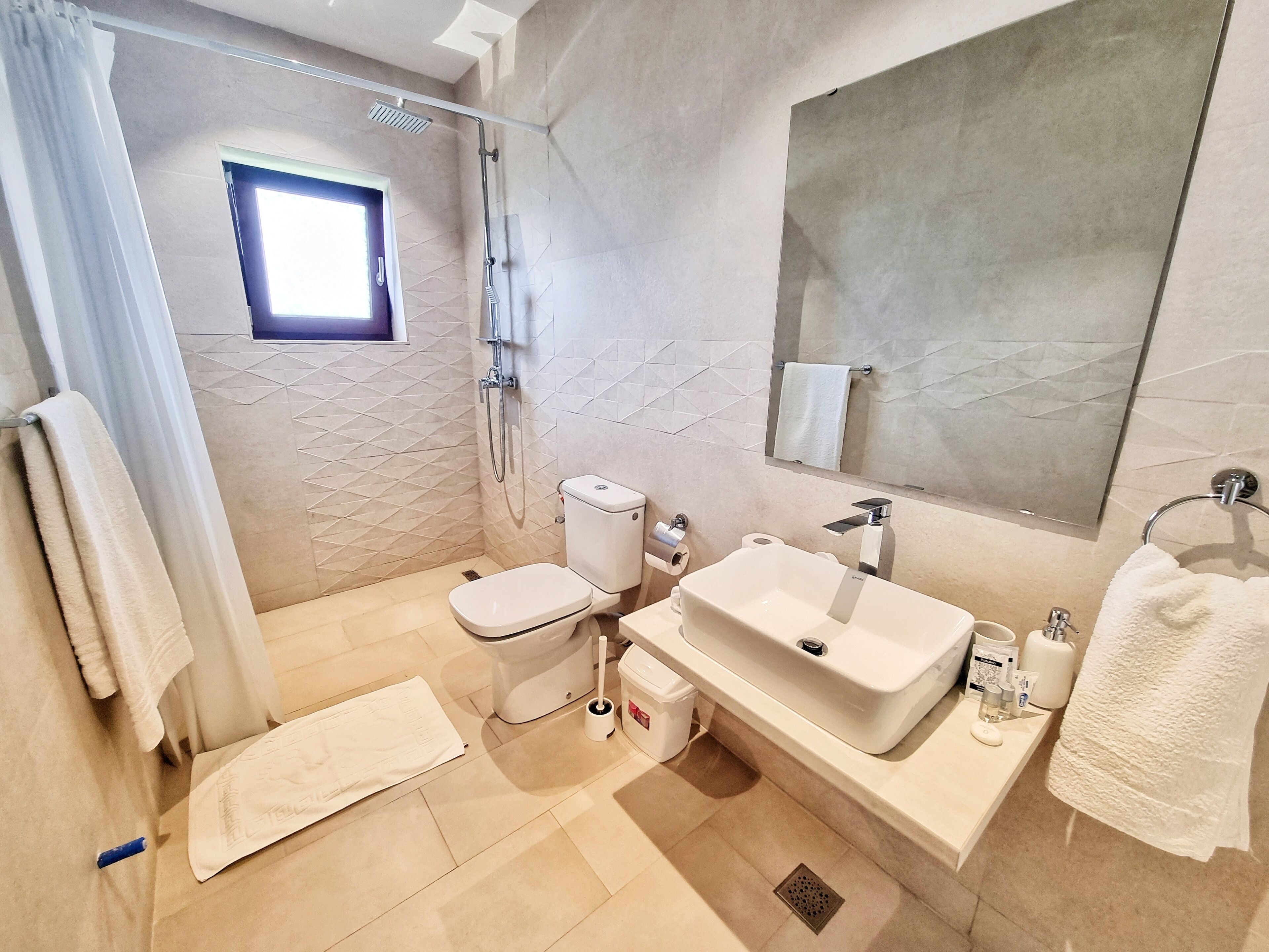 A modern bathroom with a toilet, sink, shower, and a large mirror.