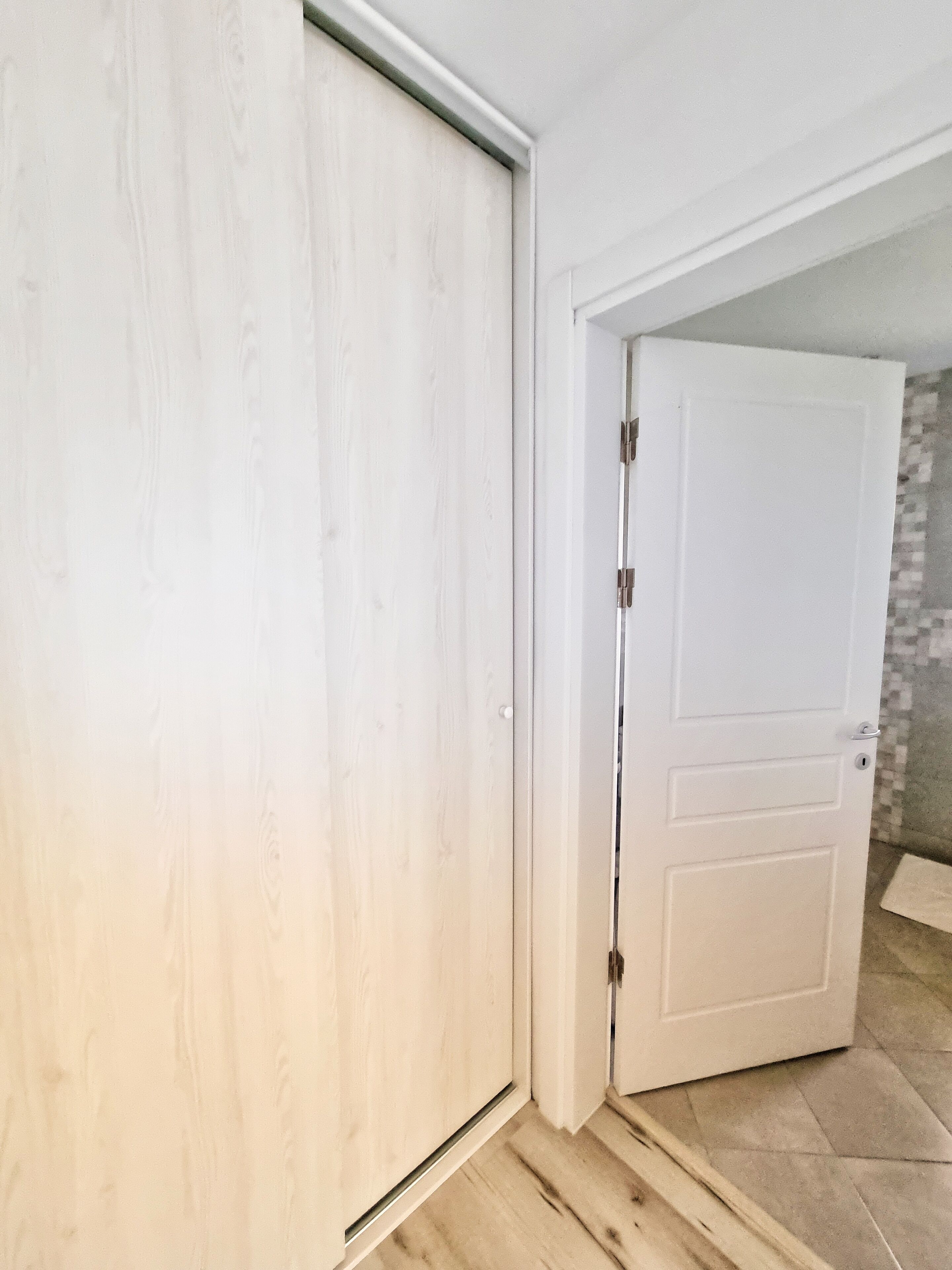 Una habitación con una puerta blanca cerrada, una puerta blanca entreabierta y un suelo de baldosas.