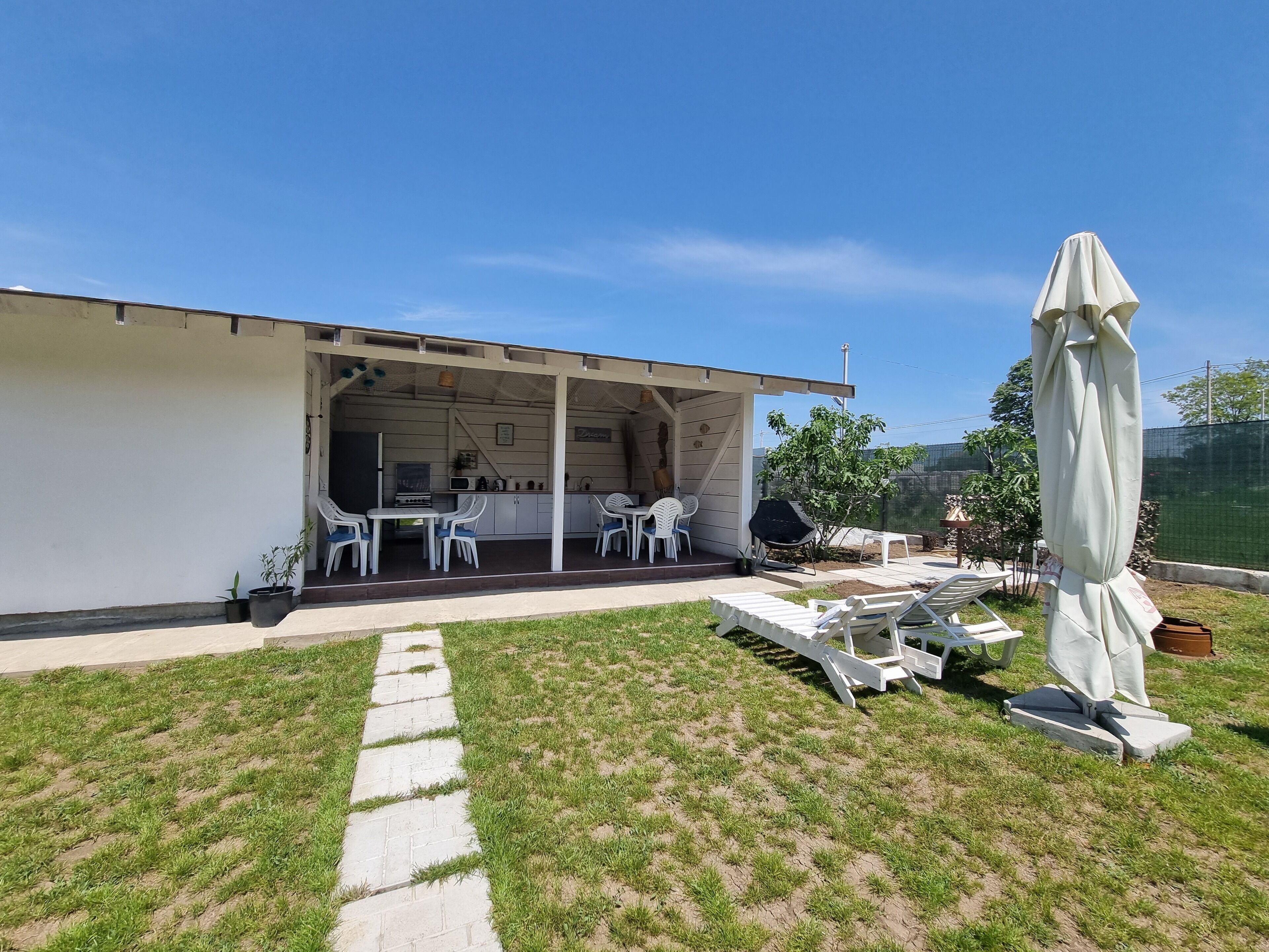 A covered patio area with a barbecue setup, outdoor seating, and a lawn.