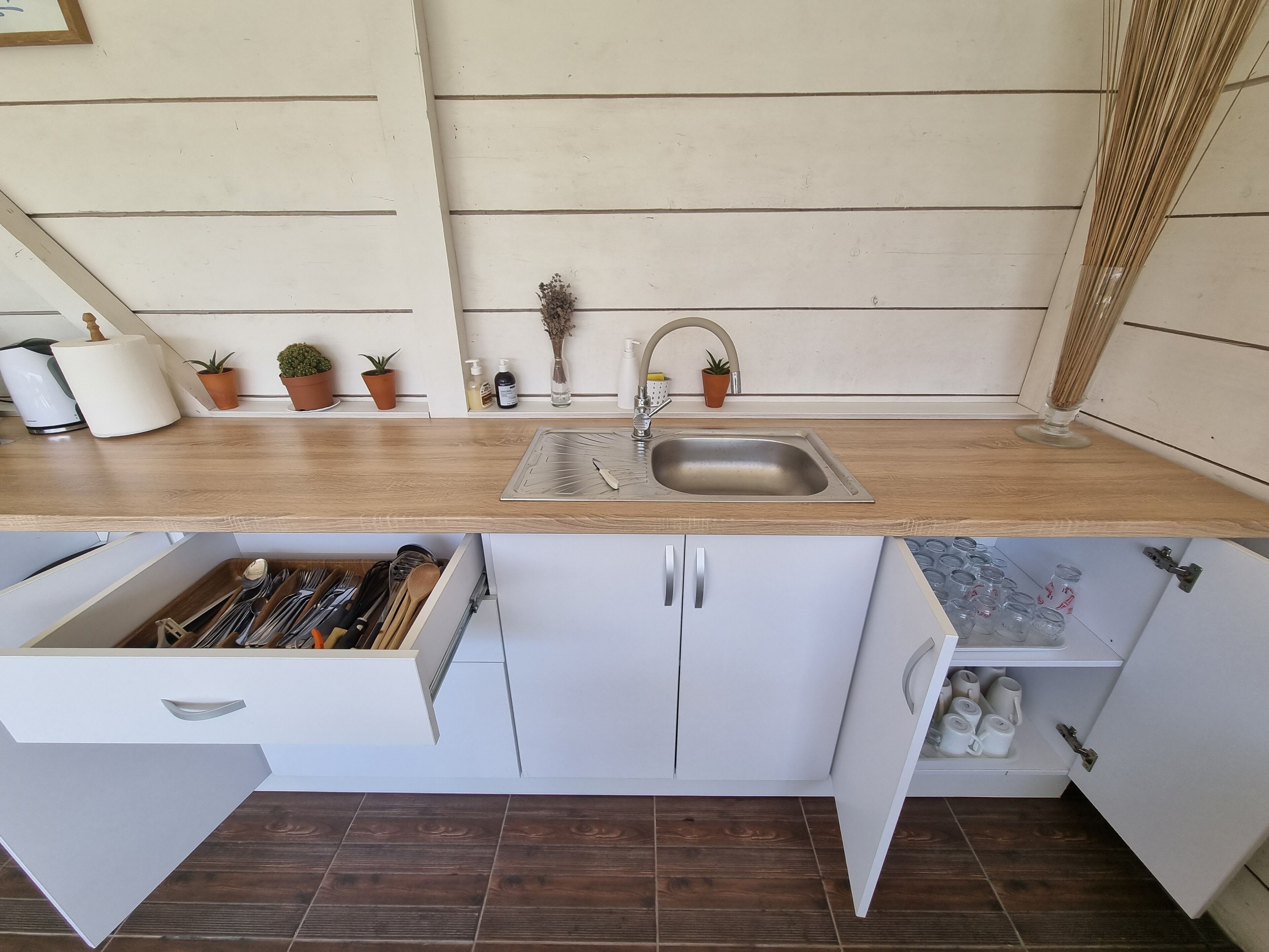 Een kleine keuken met een houten aanrecht, een roestvrijstalen spoelbak en witte kastjes.