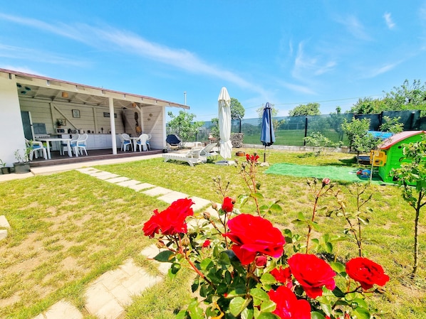 A backyard with a patio, outdoor seating, a play area, and a garden with red roses.