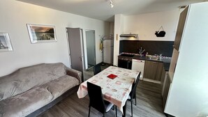 A compact living space with a sofa, a dining table with chairs, a kitchenette, and a door leading to another room. - Mountain View Flat for 5 in Mont-dore (Mont-Dore)