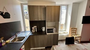 A compact kitchen with a sink, coffee maker, and microwave. There is a window with a view of buildings outside. - Mountain View Flat for 5 in Mont-dore (Mont-Dore)